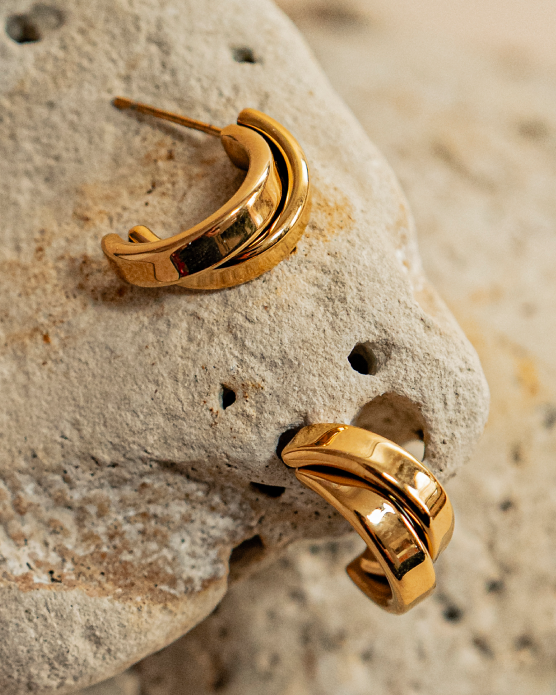 Gold wave hoops resting on a sea stone